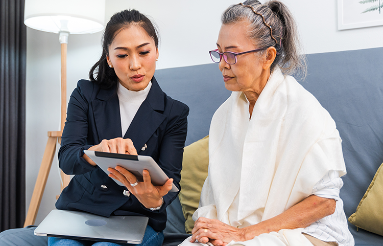 A younger woman is pointing to something on a tablet for an older woman to see.